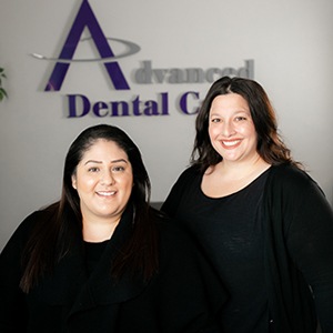 receptionists smiling in front of logo at front desk