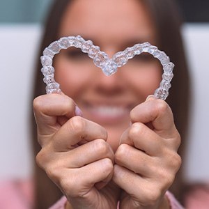 A woman making a heart with her Invisalign aligners