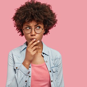 Woman wondering about cosmetic dentistry in Costa Mesa on pink background