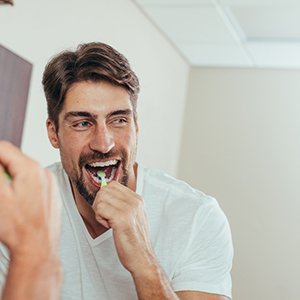 Man in white shirt brushing teeth in mirror