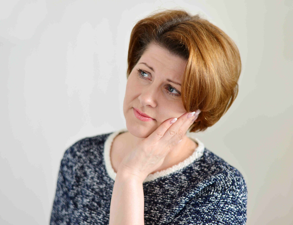 Woman in sweater rubbing jaw looking concerned