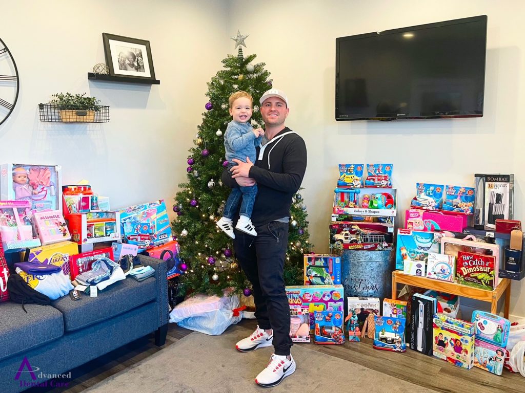 Dr. Jeremy Jorgenson and son in front of Christmas gifts for Project Self Sufficiency OC.
